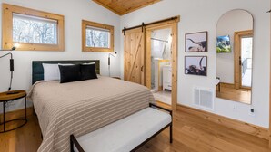 A bedroom with a bed, a desk, a chair, a window, a mirror, and a sliding door. - Modern Mountain Lodge with a View (Fleetwood)