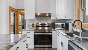 A modern kitchen with white cabinets, stainless steel appliances, and a herringbone tile backsplash. - Modern Mountain Lodge with a View (Fleetwood)