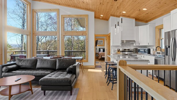 A modern kitchen with white cabinets, stainless steel appliances, and large windows offering a view of trees. - Modern Mountain Lodge with a View (Fleetwood)