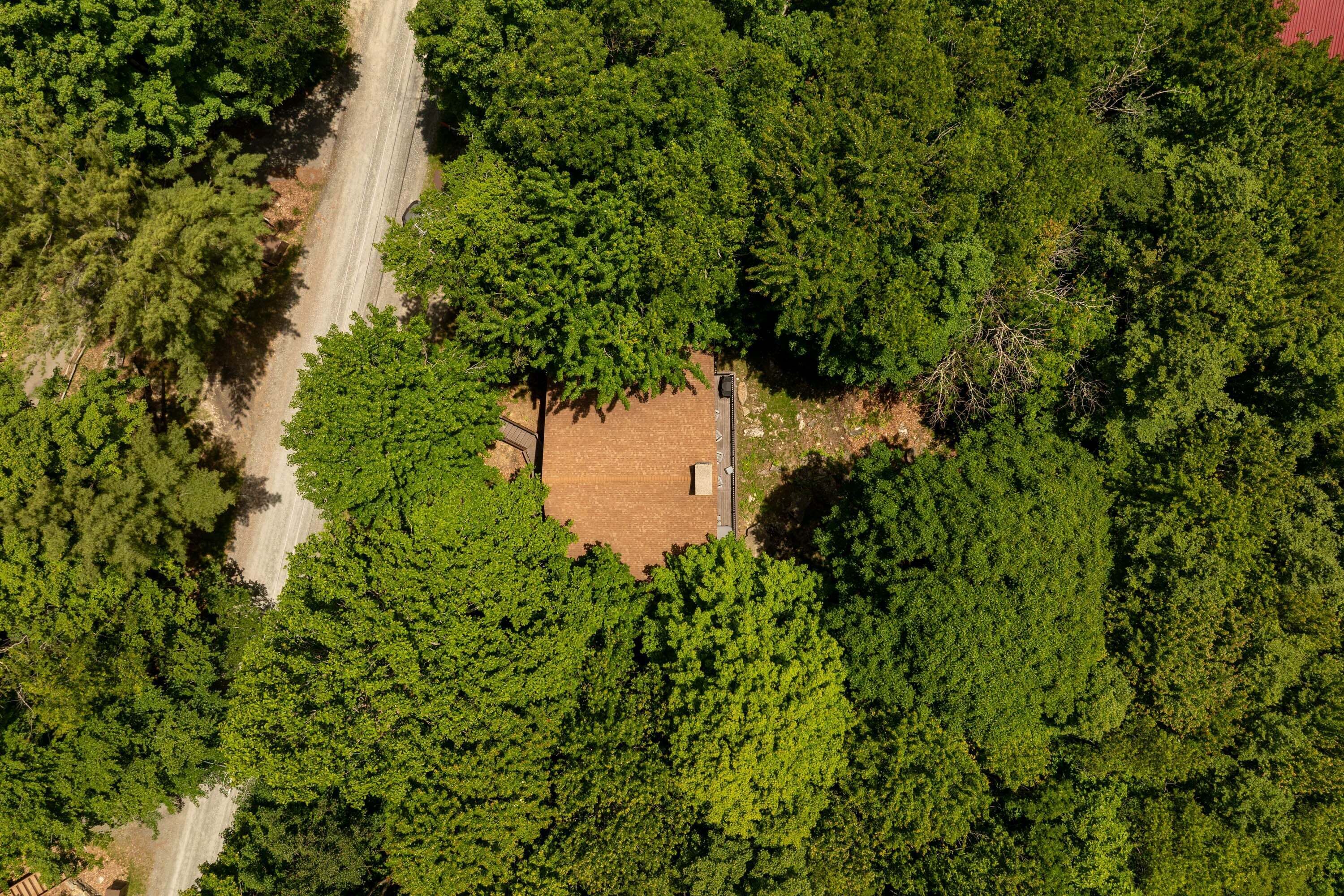 An aerial view of a forested area with a rectangular building surrounded by dense trees.
