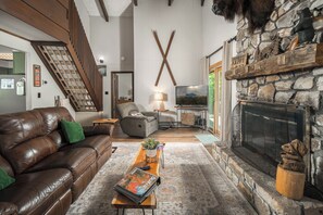 Un salon chaleureux avec un canapé en cuir, une cheminée en pierre, un téléviseur et un escalier.