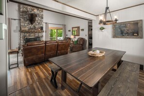 A rustic interior with a stone fireplace, leather seating, a wooden dining table, and a chalkboard sign.