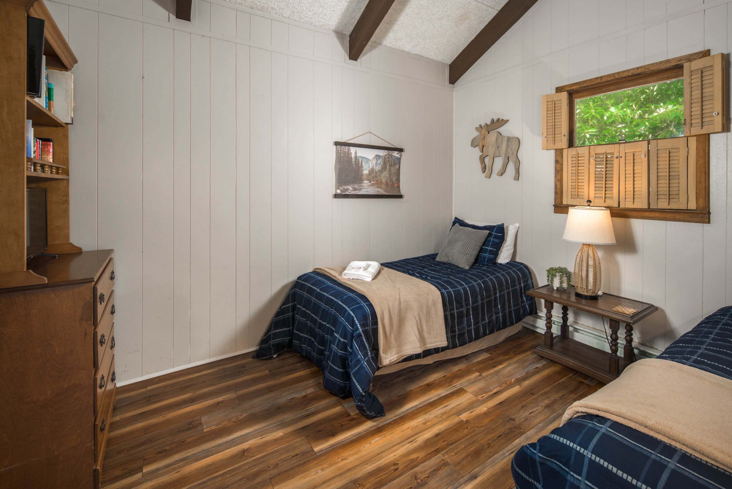 Ein Schlafzimmer mit zwei Betten, Holzboden, einem Wandbild, einem Holzregal mit Büchern und einem aufgehängten Tierkopf.