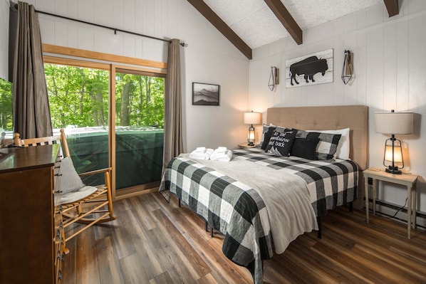 A bedroom with a bed, two bedside tables with lamps, a chair, a desk, and a window with curtains.