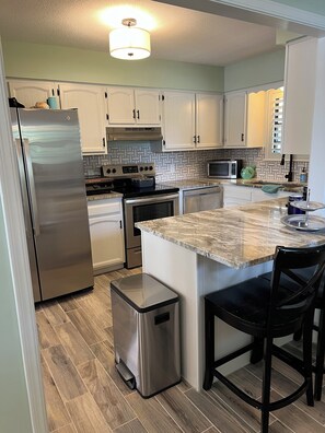A kitchen with white cabinets, stainless steel appliances, a granite countertop, and a small trash bin. - Ketchum Cove Family & Pet-Friendly Lake House w/ Dock & Walk to Marina Dining (Vinita)