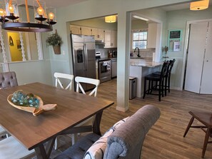 A modern kitchen with a stainless steel refrigerator, a dining area with a wooden table and white chairs, and a cozy seating area with a cushioned bench. - Ketchum Cove Family & Pet-Friendly Lake House w/ Dock & Walk to Marina Dining (Vinita)