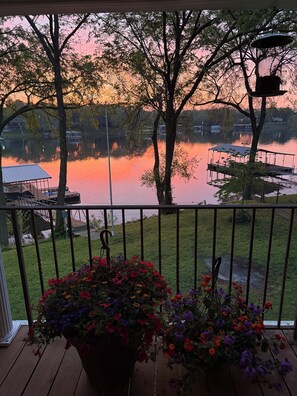 A balcony with a view of a lake at sunset, a dock, and a flower pot.