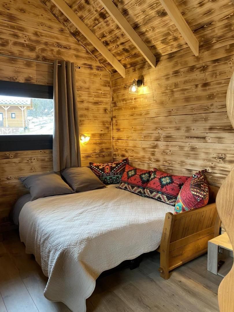 A cozy wooden room with a bed, a window with curtains, and a small table.