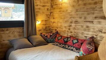 A cozy wooden room with a bed, a window with curtains, and a small table.