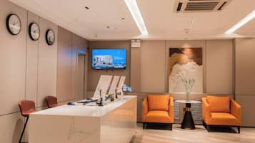 Un área de recepción con mostrador de mármol, dos sillas anaranjadas, un televisor y un reloj de pared.