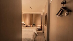Habitación de hotel con dos camas, una mesita de noche, una silla, un escritorio, perchero y televisor montado en la pared.