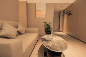 Un salon moderne avec un canapé, une table basse en marbre, une plante en pot et une œuvre d’art murale aux lignes épurées.