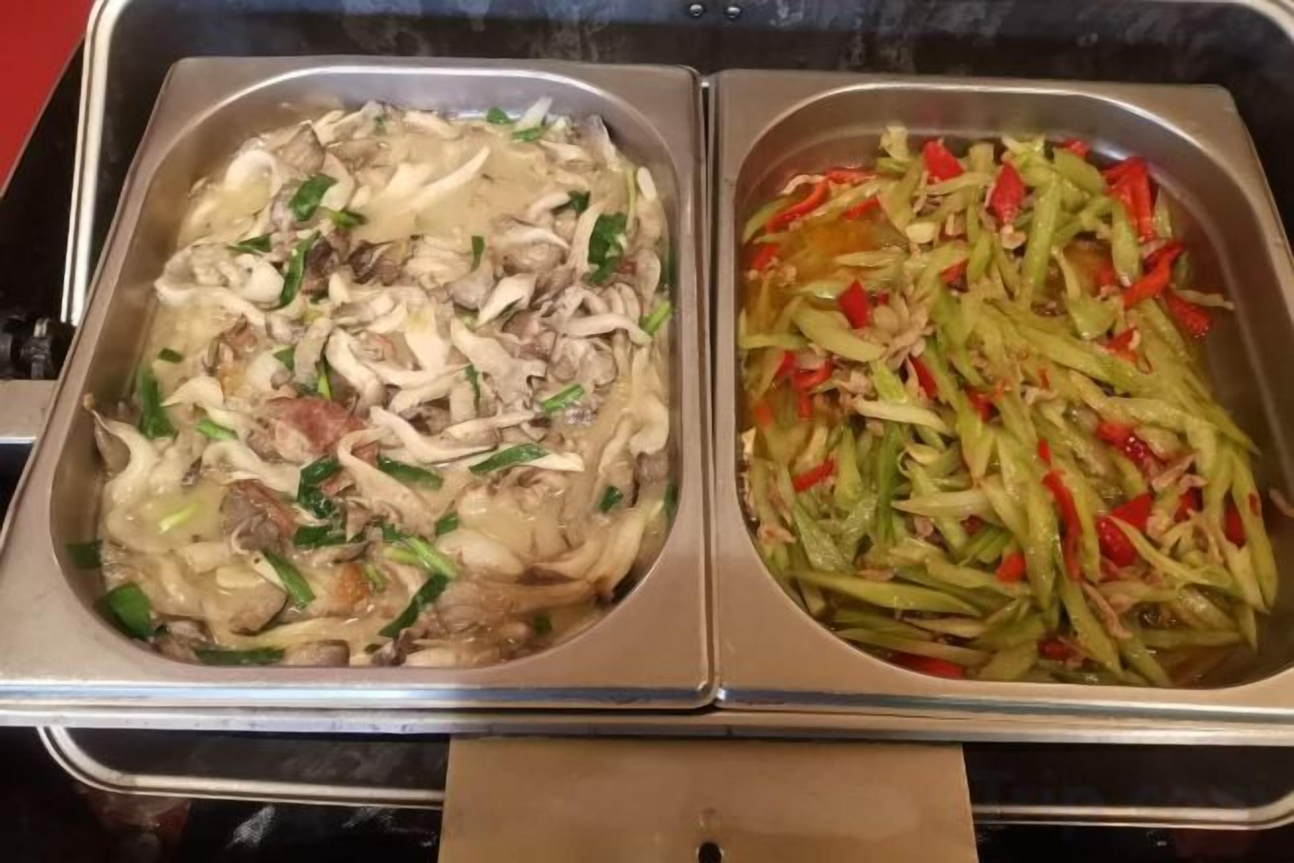 A buffet with two sections; one with a creamy soup containing vegetables and meat, and another with sliced green vegetables and red peppers.
