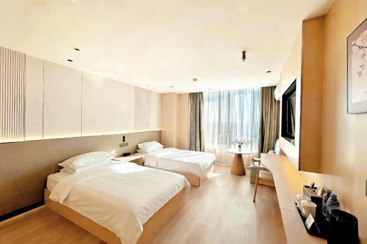 A hotel room with two beds, a desk, a chair, a TV, and a window with curtains.