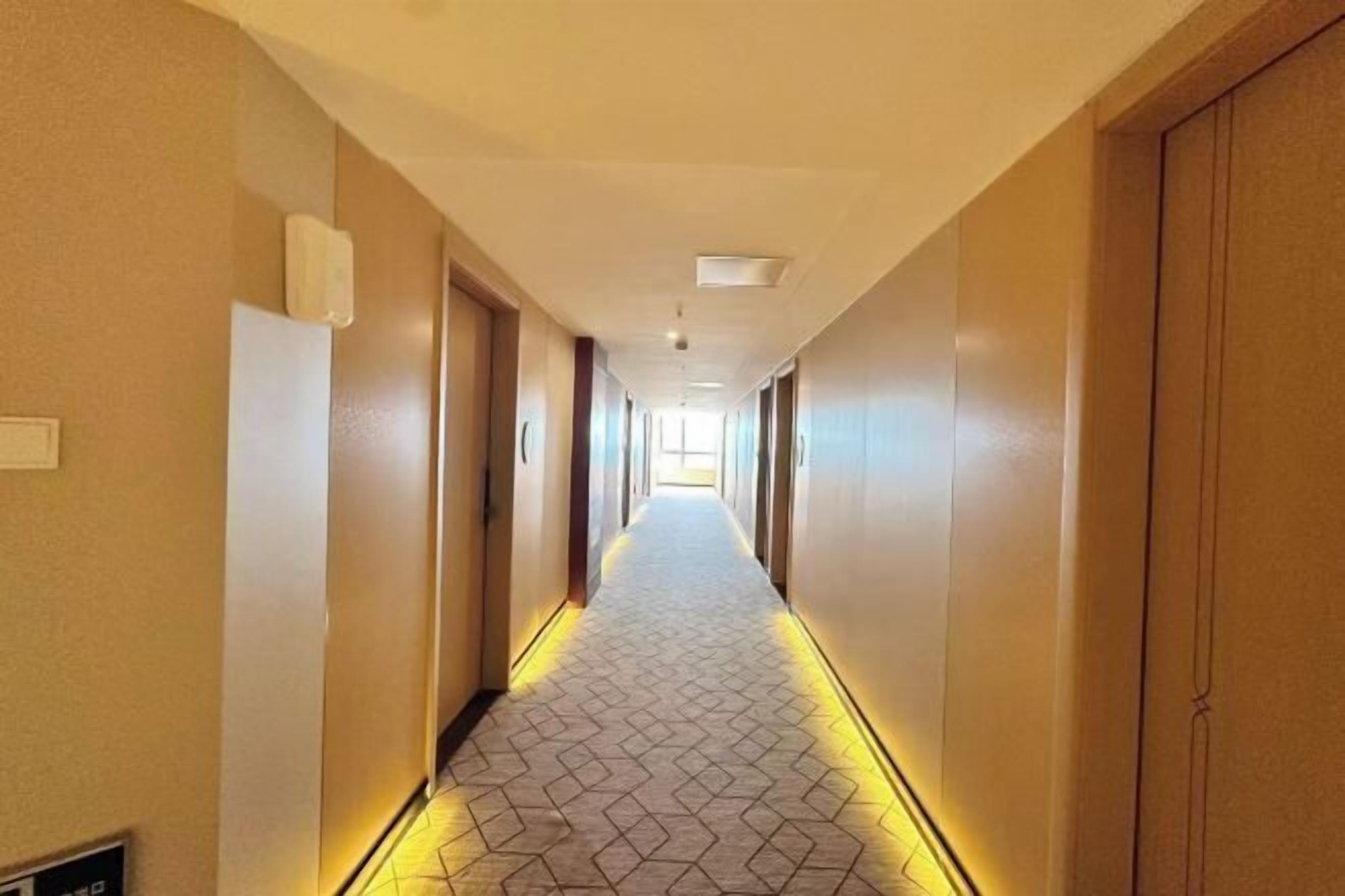 A hotel corridor with a patterned floor, doors on both sides, and a long hallway leading to a bright end.