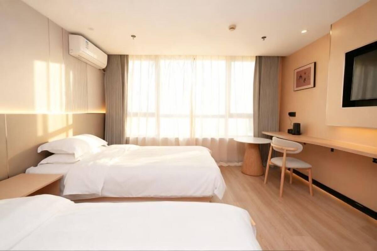 A hotel room with two beds, a desk, a chair, and a TV.
