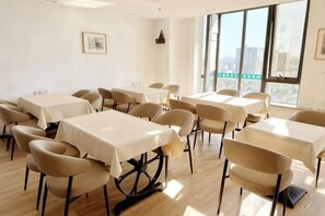 A conference room with multiple tables and chairs, large windows with a view of buildings, and a framed picture on the wall.