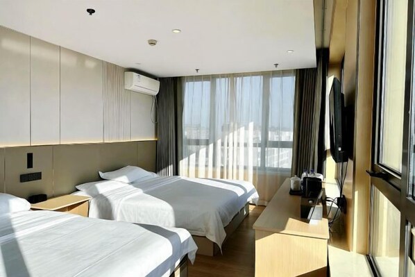 Habitación de hotel con dos camas, un escritorio, un televisor y ventanas amplias.