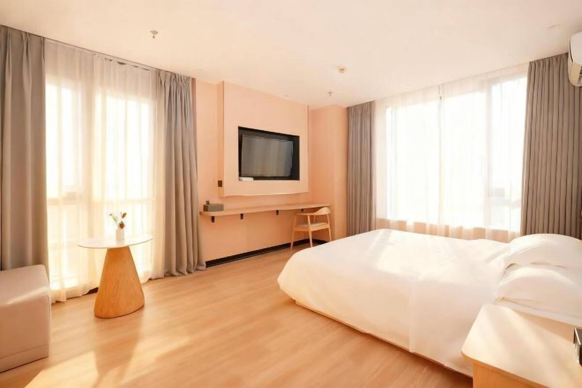 A hotel room with a bed, a desk, a chair, a TV, and a small table.