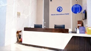 A reception desk at Wenfei International Hotel with a marble wall, a logo, and a digital information board. - Shanghai Wenfei Boutique Hotel (Shanghai)