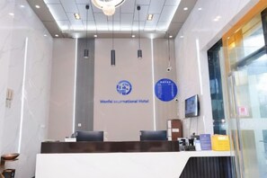 A reception area with a reception desk, two chairs, a wall-mounted TV, and a logo for Wenfei International Hotel.