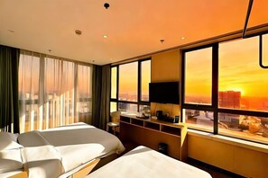 A hotel room with two beds, a desk, a chair, a TV, and a large window with a city view.