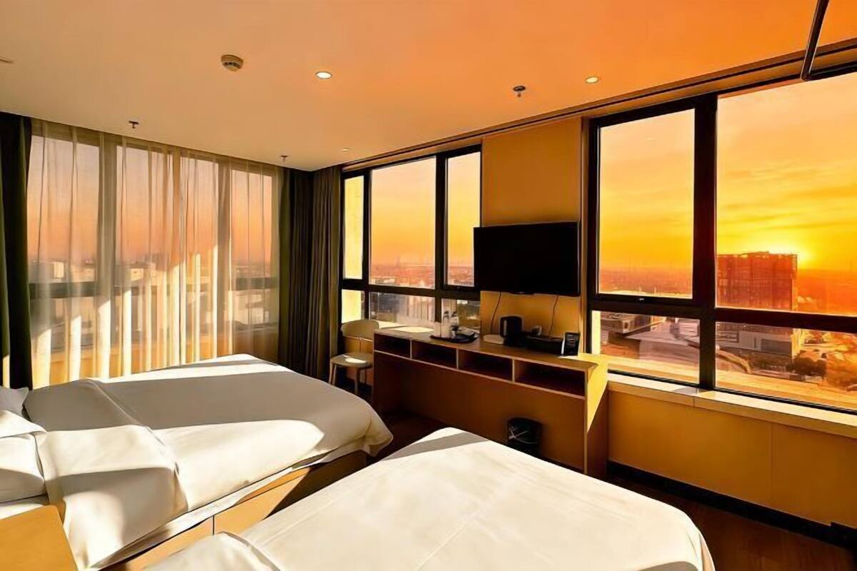 A hotel room with two beds, a desk, a chair, and a TV.