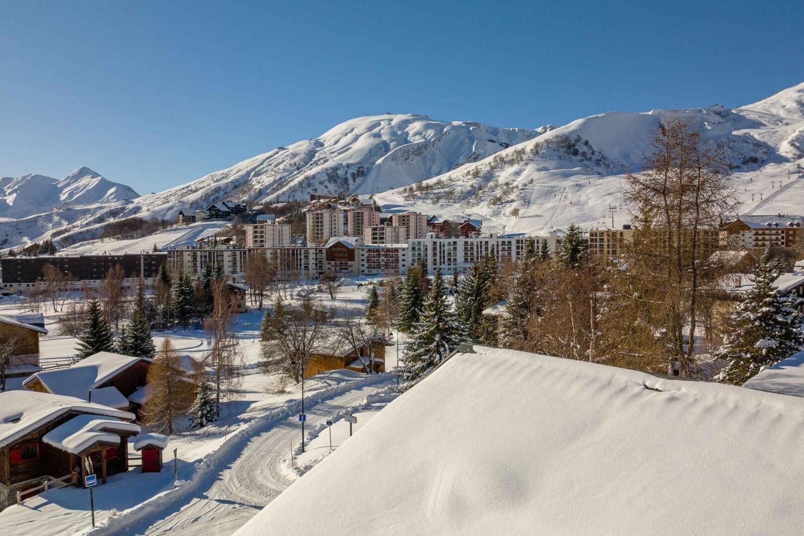 Una località montana innevata con diversi edifici, tra cui un grande albergo e una seggiovia sullo sfondo.