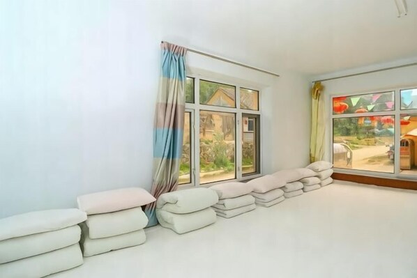 A room with a large window, a view of a garden, and a stack of towels against the wall.