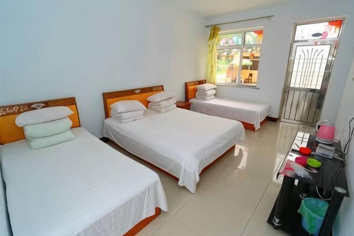 Quarto de hotel com três camas de solteiro, uma mesinha com produtos de higiene pessoal e uma janela com vista.