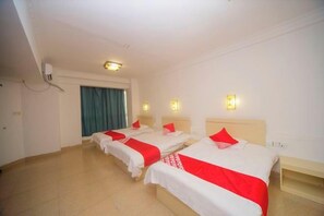 A hotel room with three beds, a desk, and a window with curtains.