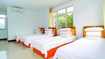Een hotelkamer met drie bedden, elk voorzien van witte beddengoed en oranje hoofdeinden, grote ramen met gordijnen en een betegelde vloer.