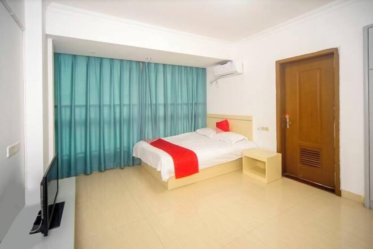 Quarto de hotel com cama, mesa de cabeceira, televisão e porta.