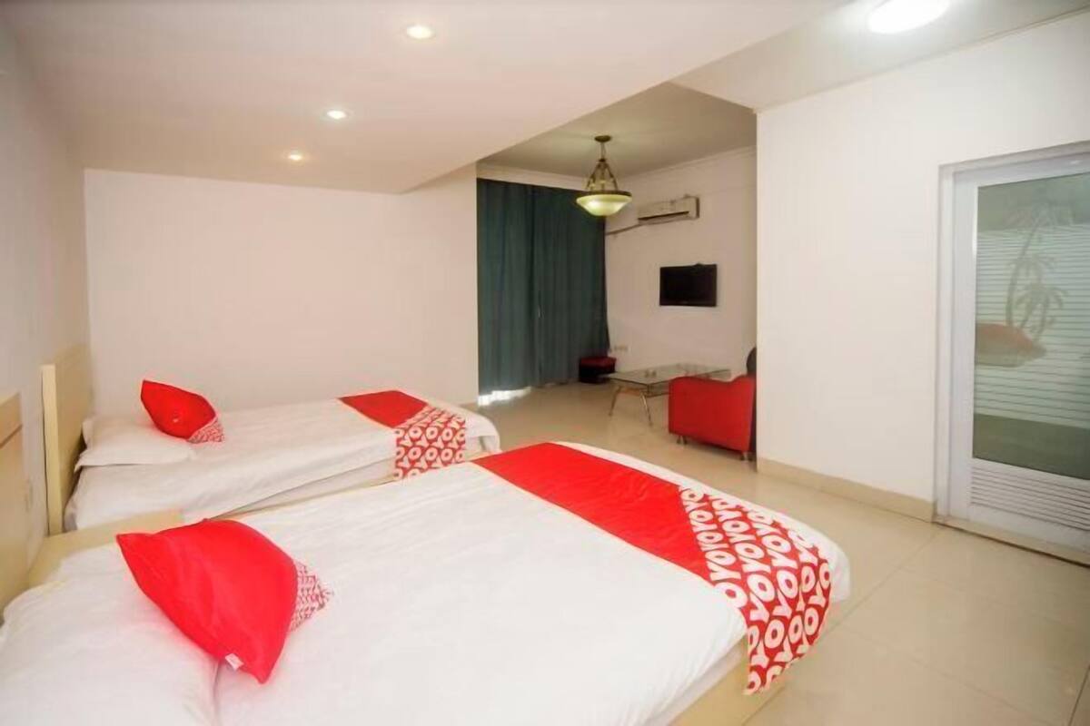 Quarto de hotel com duas camas, uma escrivaninha, uma cadeira, uma janela e uma porta.