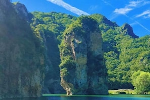 A natural landscape with a prominent rock formation surrounded by lush greenery and a clear blue sky.