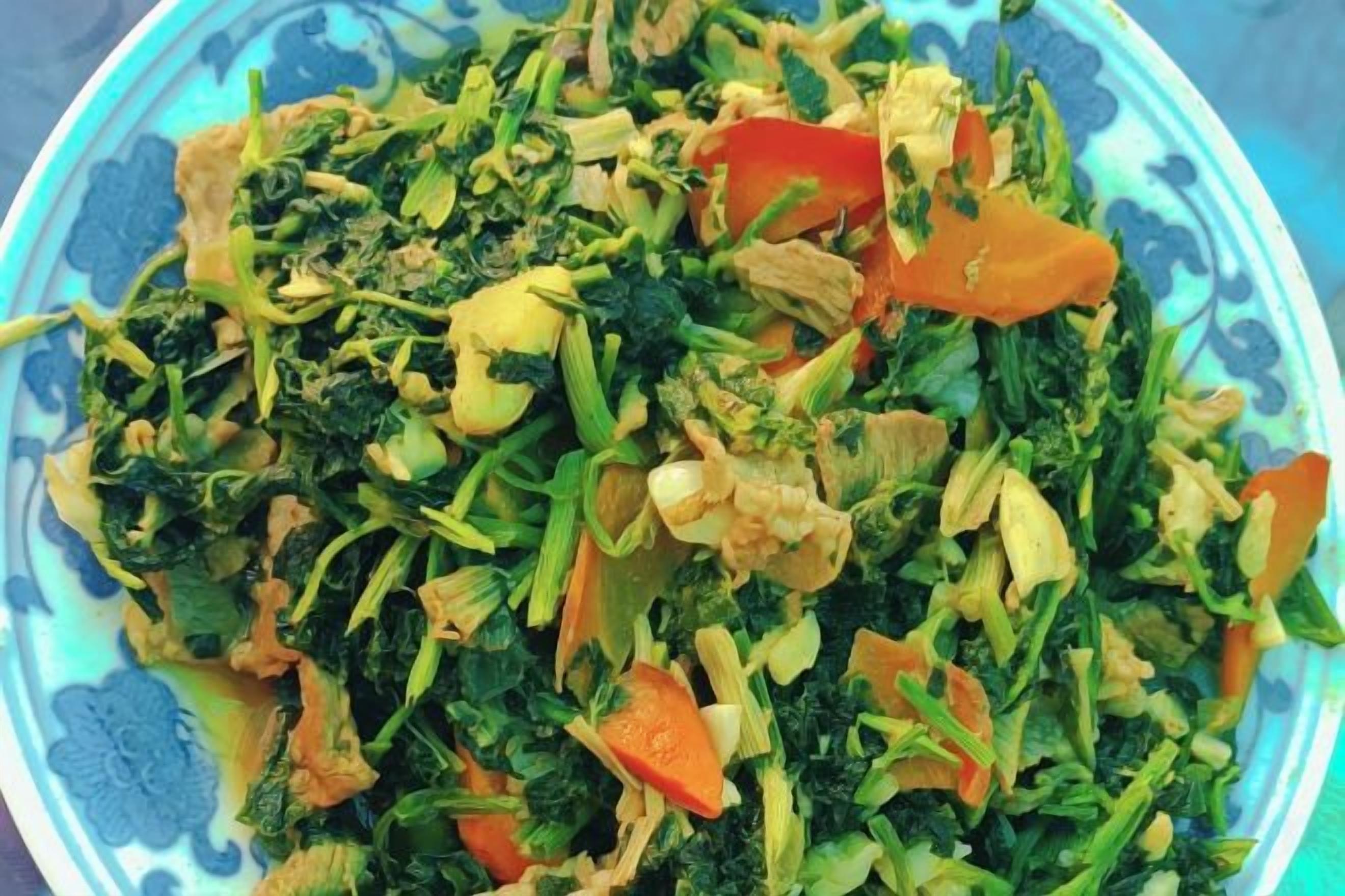 A bowl of mixed vegetables including carrots and leafy greens.