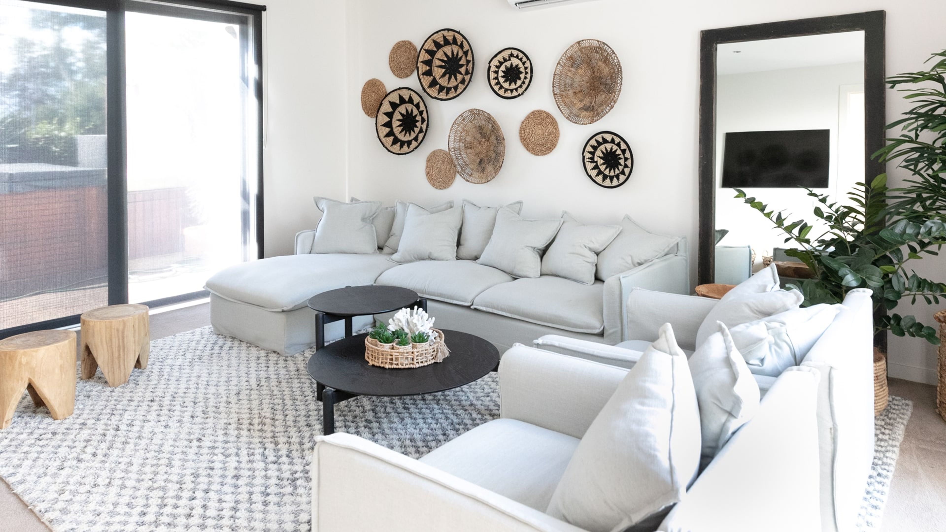A modern living room with a sectional sofa, a round coffee table, and decorative woven wall art.