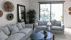 Una sala de estar con un sofá gris, una mesa de centro redonda y un ventanal con vistas a zonas verdes.
