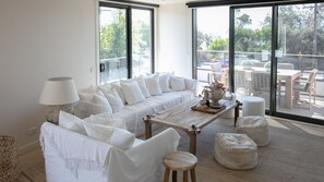 A modern living room with a sofa, a coffee table, and a lamp. There are large windows offering a view of the outdoors. - Stunning Beach Views Pet Friendly Dromana Retreat (Dromana)
