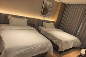 Habitación de hotel con dos camas, cabecero, una obra de arte colgada en la pared y ventana con cortinas.