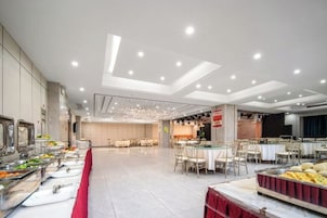 Un amplio comedor con varias mesas y sillas, una barra de buffet con diferentes opciones de comida y un diseño moderno en el techo.