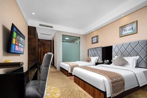 Habitación de hotel con dos camas, un escritorio, una silla, un televisor y un cuadro en la pared.