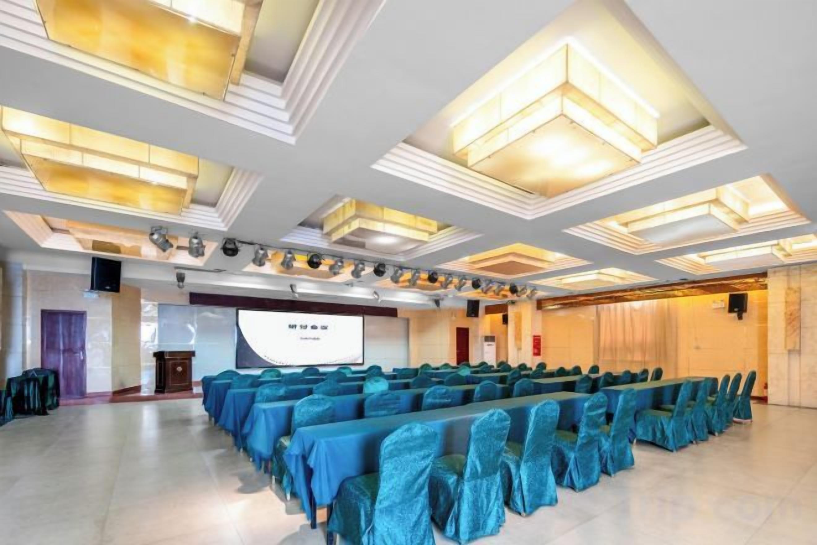 A conference room with rows of chairs, a projection screen, and a stage with lighting.
