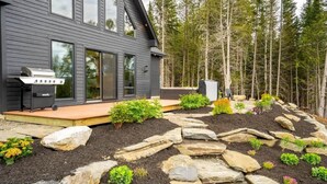 Una casa moderna con una terraza amplia, una parrilla y un sendero de piedra que conduce a la entrada.