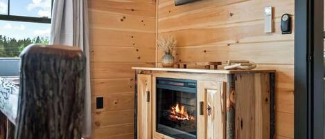 Ein gemütliches Blockhaus-Interieur mit Holzvertäfelung, Kamin, Wand-Fernseher und Fenster mit Blick ins Freie.