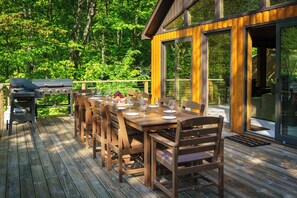 Une terrasse en bois avec une table et des chaises, un barbecue et une porte vitrée donnant sur un espace abrité.