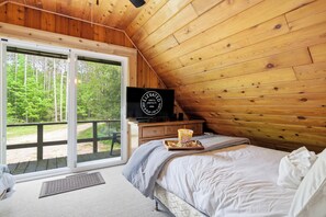 Une chambre à coucher avec un lit, une télévision, une fenêtre donnant sur des arbres et un plafond en bois.