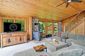 Un intérieur en bois avec une cheminée en pierre, un téléviseur posé sur un meuble en bois et un canapé gris.