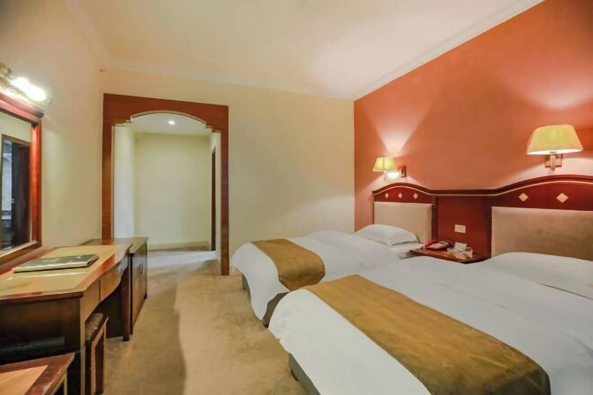A hotel room with two beds, a desk, and a mirror.