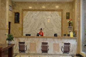 A marble reception desk with a receptionist, three chairs, and a potted plant. - Libo Dapeng Business Hotel (Libo Ancient Town) (Libo)